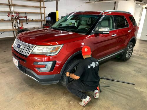 Person kneeling beside a red SUV in a garage, inspecting the front wheel area