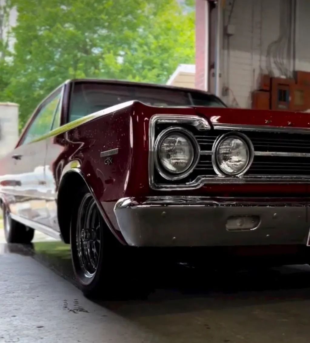 Classic maroon muscle car parked in a garage, front-left view with chrome grille and headlights.
