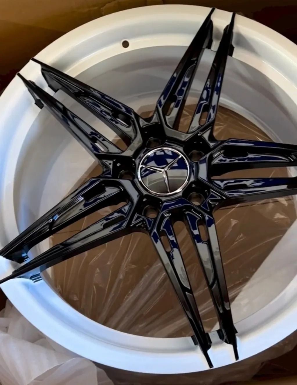 Black star-shaped wheel rim with chrome accents, resting in a white container with plastic wrap.