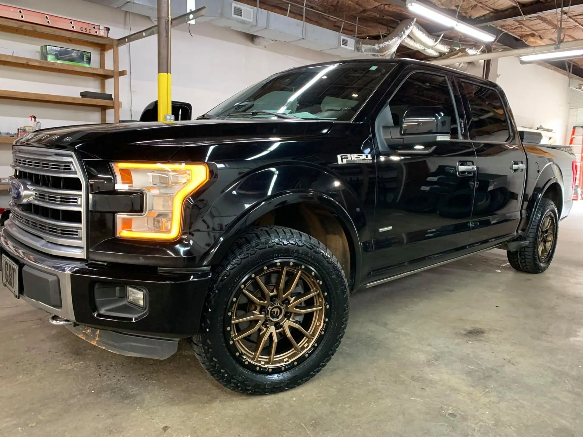 Black Ford F-150 in a garage, with gold wheels and amber headlights on