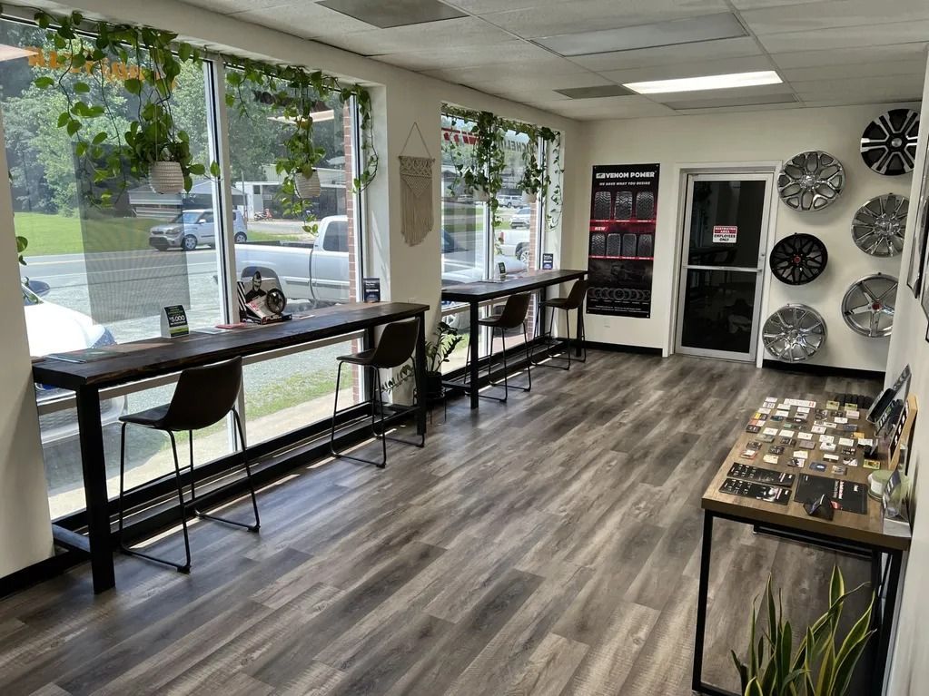 Empty retail showroom with wood floors, display tables, large windows, and wall-mounted tire displays