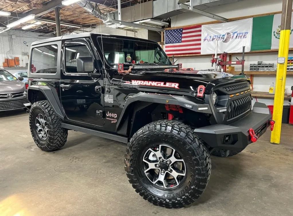 Black lifted Jeep Wrangler with oversized tires in a garage, shown side view.