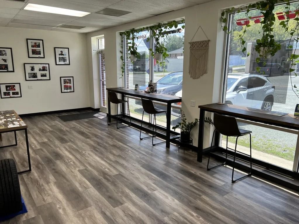 Bright room with wood floors, large windows, stools, tables, and hanging greenery.