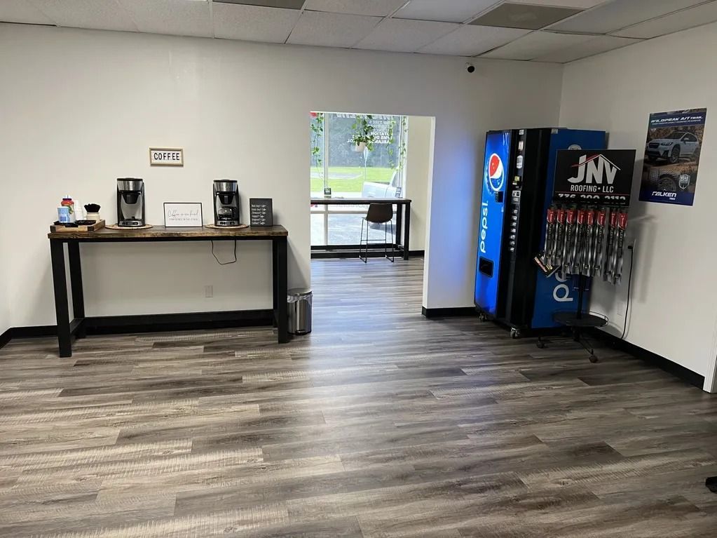 Empty break room with a table, coffee station, vending machine, and jacket rack near a doorway