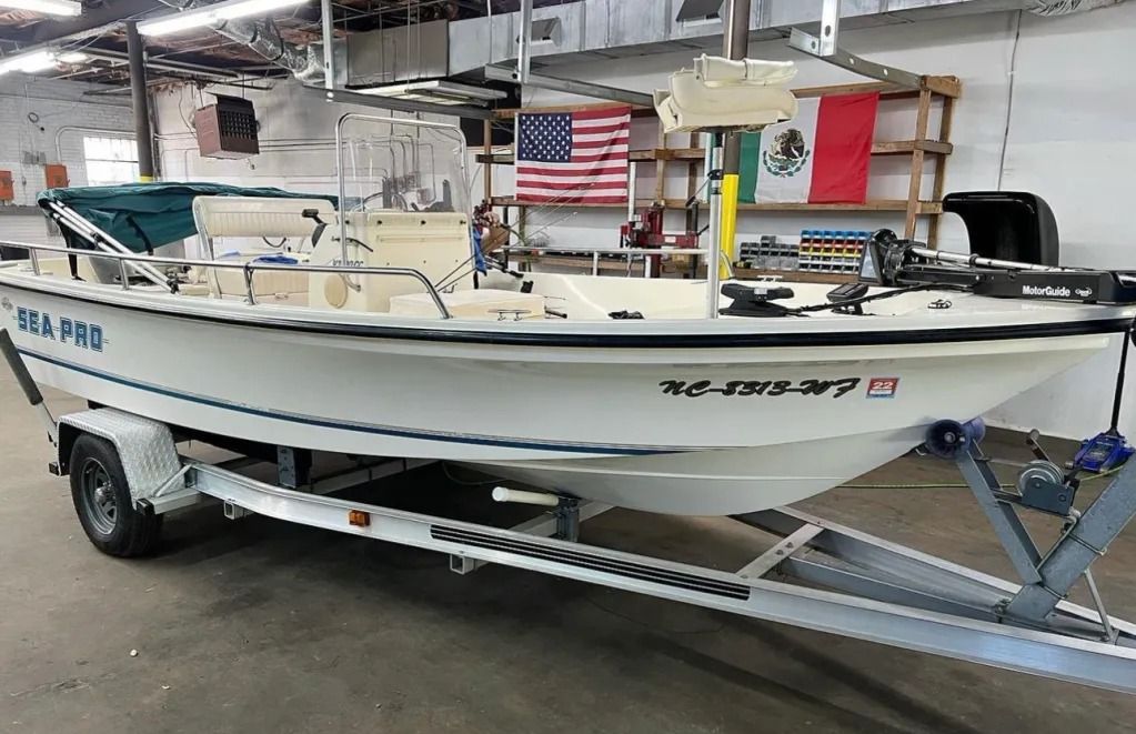 White fishing boat on a trailer in a warehouse, with flags mounted on deck.