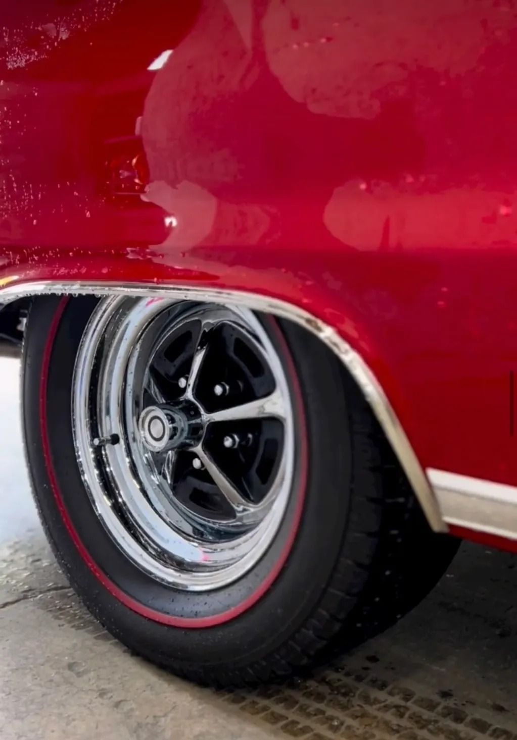 Close-up of a red classic car’s rear wheel with chrome rim and black tire on pavement