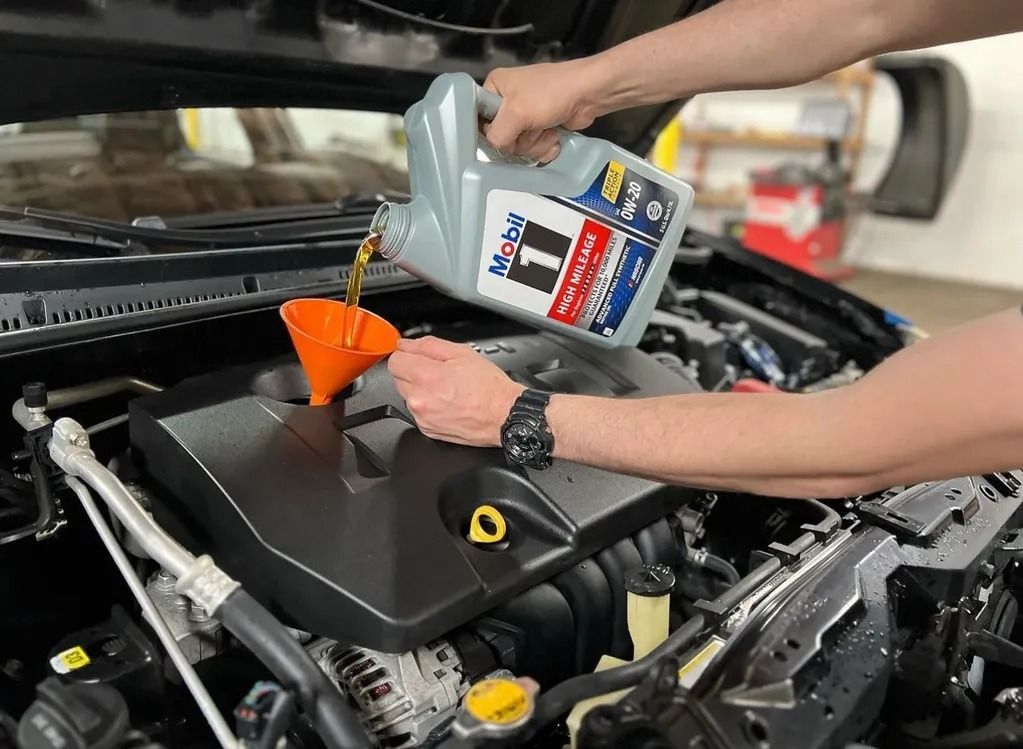 Pouring motor oil into a car engine through a funnel under the hood