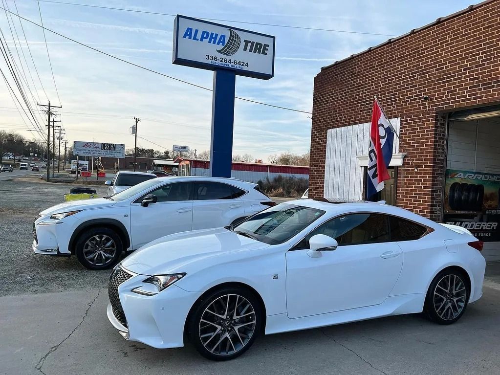 Two white cars parked outside a dealership with a sign and brick building in the background