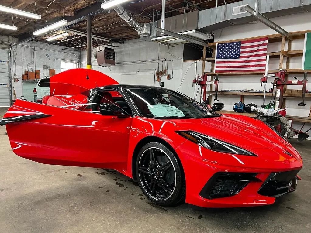 Red sports car with driver-side door open inside an industrial garage, American flag in the background