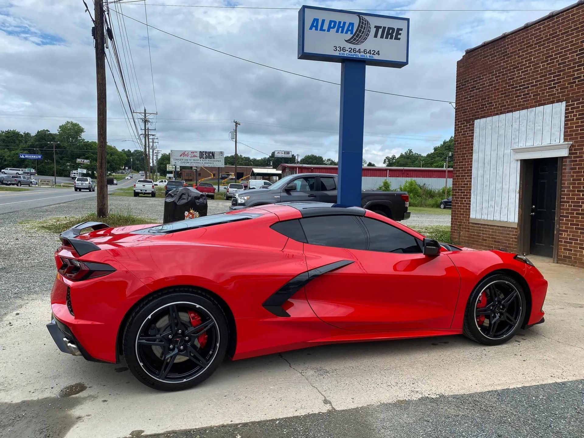 Red sports car parked outside Alpha Tire shop on a cloudy day