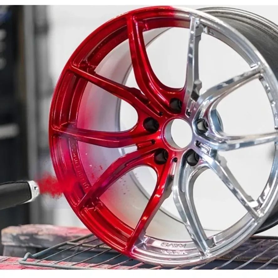Red and silver car wheel rim being spray painted in a workshop