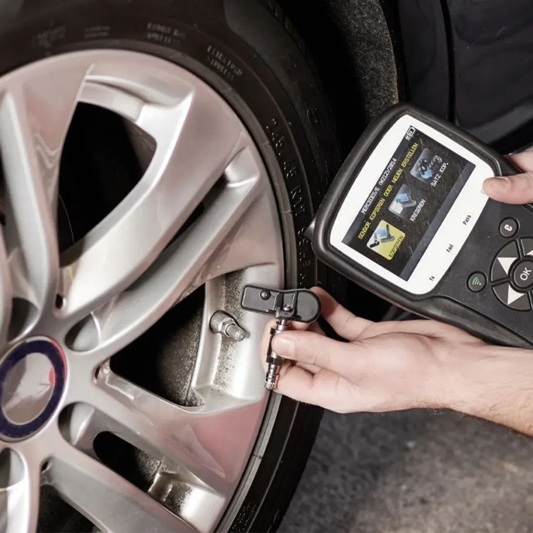 Technician using a digital wheel balancer on a silver car rim in a garage