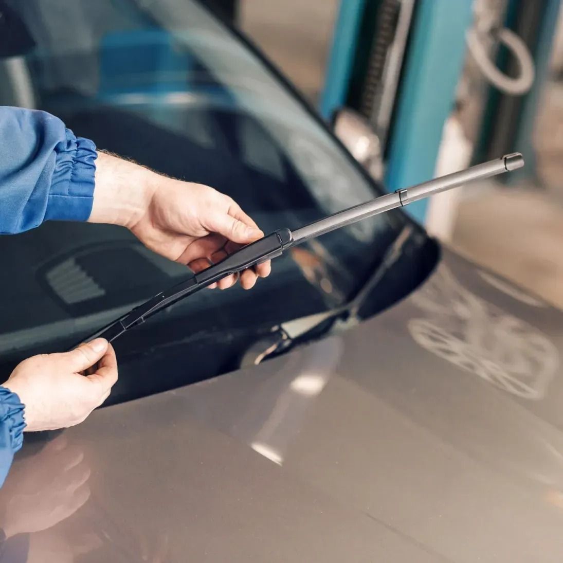 Hands holding a windshield wiper blade over a car windshield
