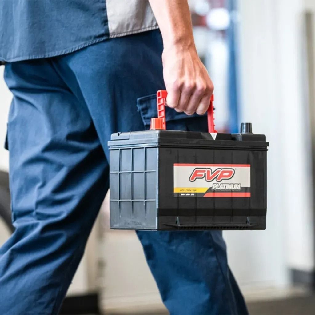 Person carrying a black FVP battery by the red handle outdoors