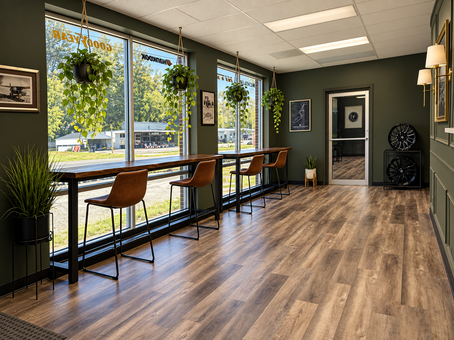 Modern office lounge with wood floors, large windows, plants, and chairs along a high counter.