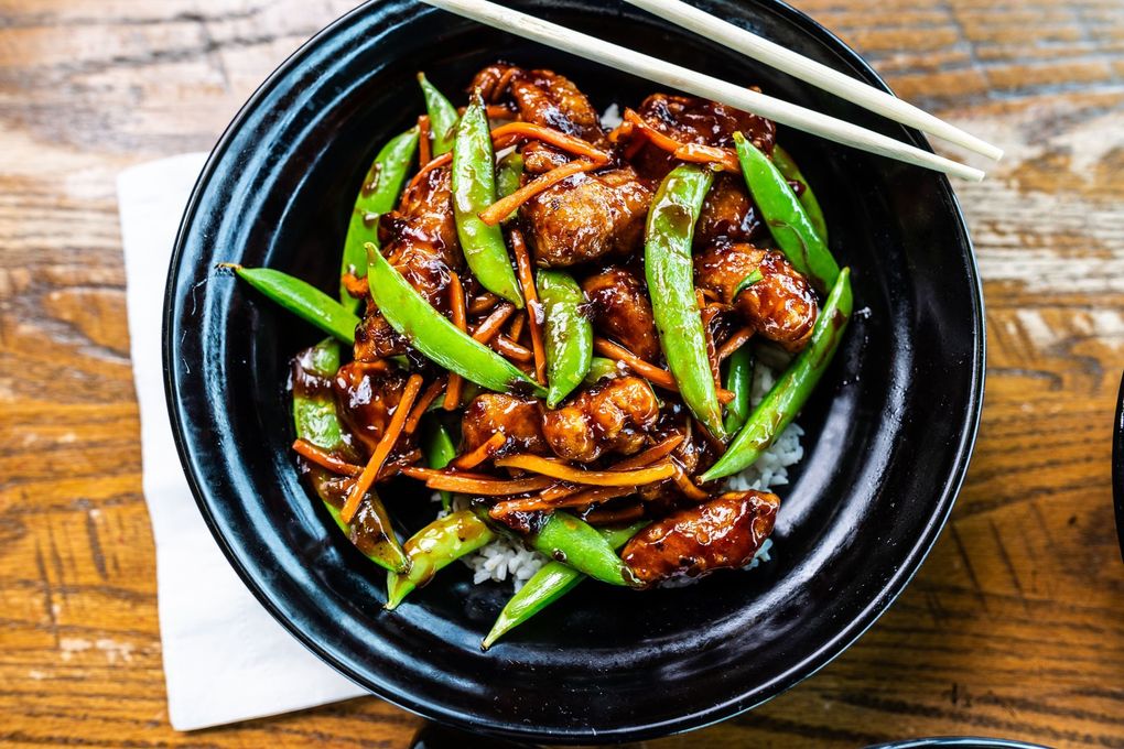 A bowl of food with chopsticks on a wooden table.