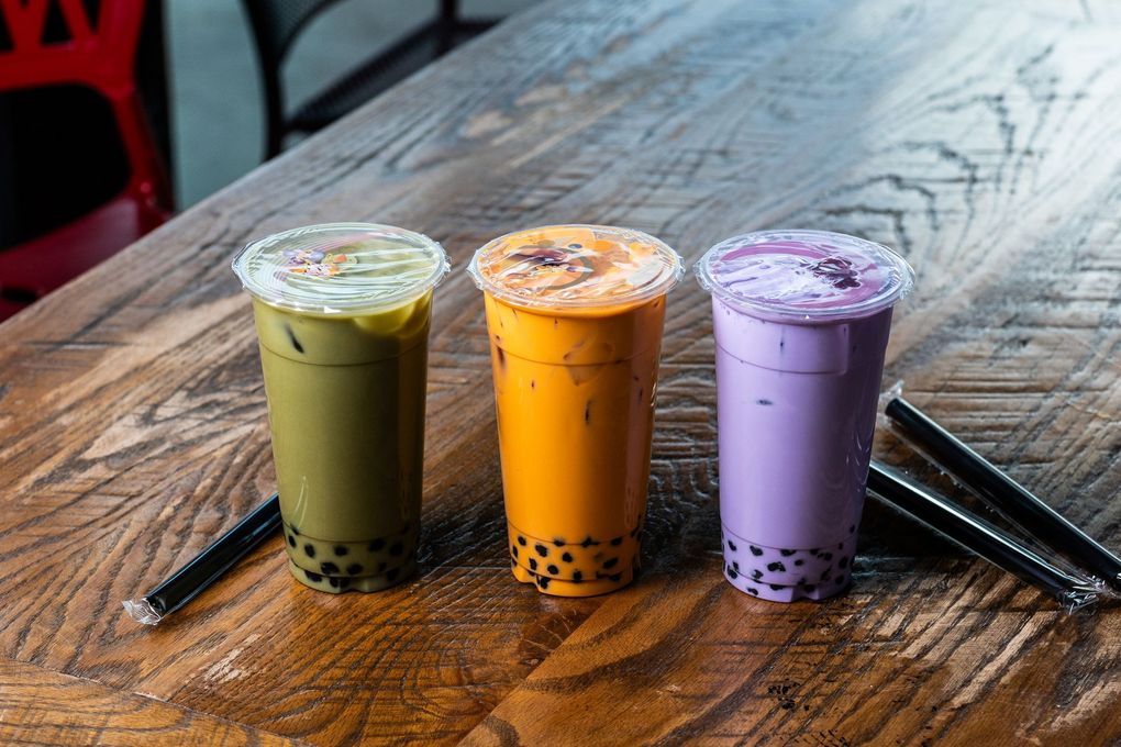 Three cups of bubble tea are sitting on a wooden table.