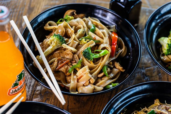 A bowl of food with chopsticks and a bottle of soda on a table.