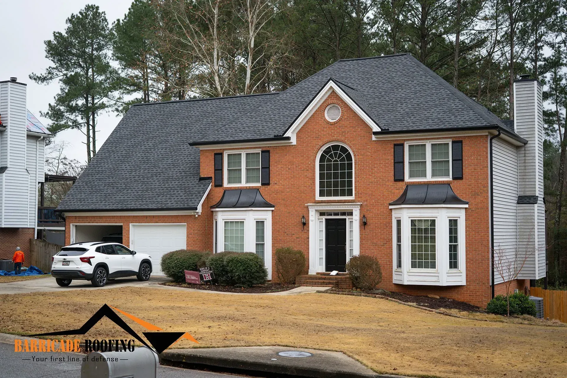 Two-story brick house with dark roof and white trim. A white car is in the driveway.