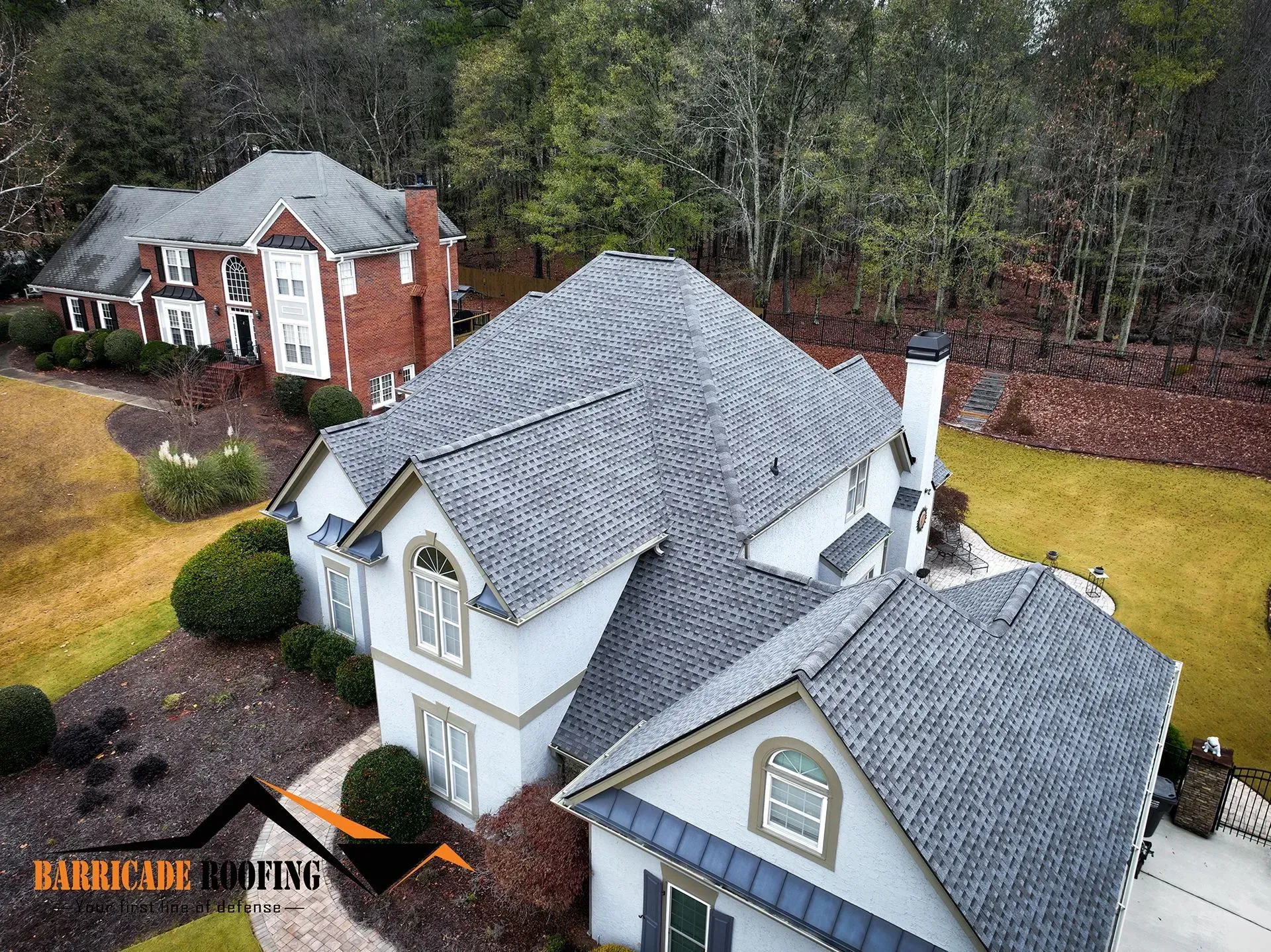 Two houses with gray roofs and green lawns, surrounded by trees.