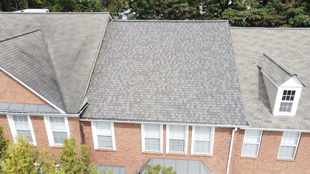 Brick building with gray shingled roof, multiple windows, and a small dormer.