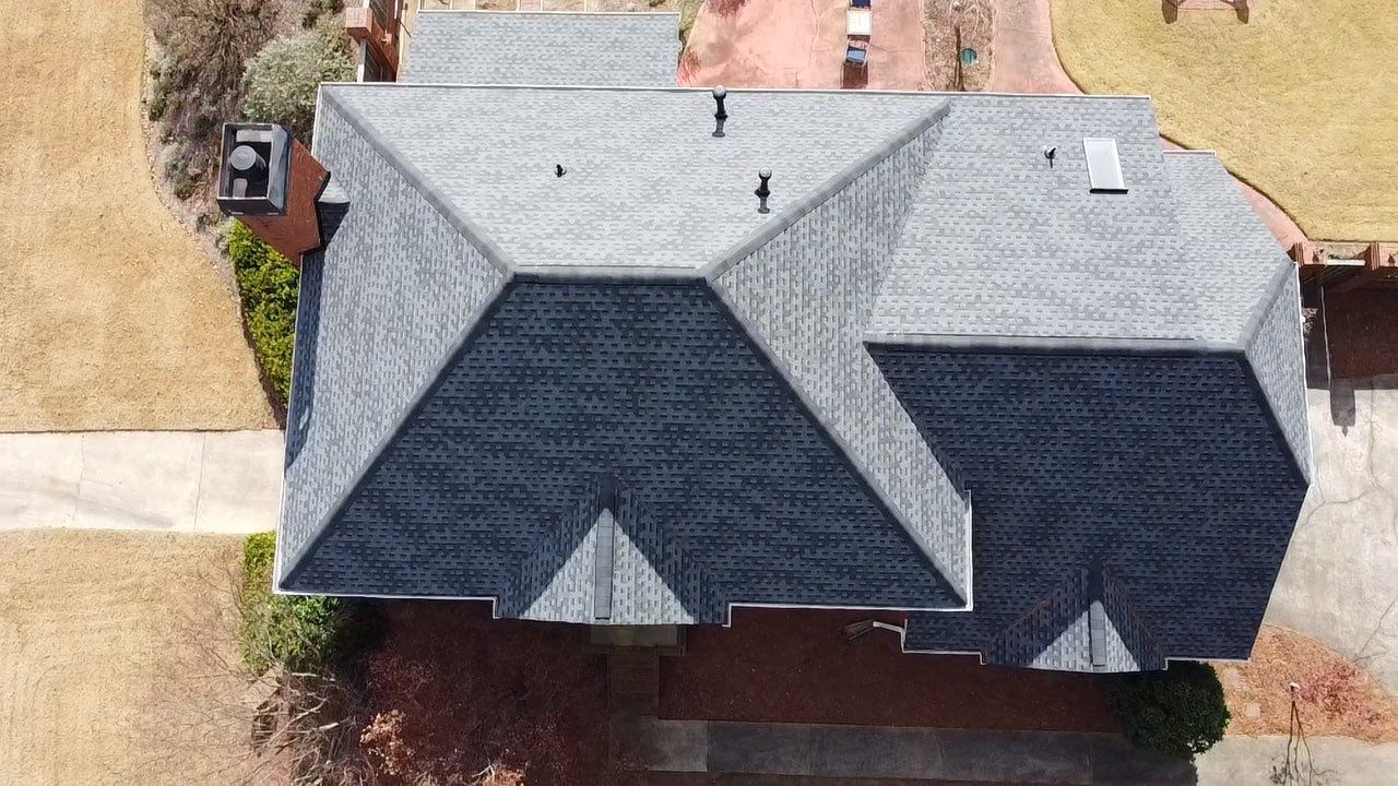 Overhead view of a house with dark gray asphalt shingle roof and chimney, in a grassy setting.