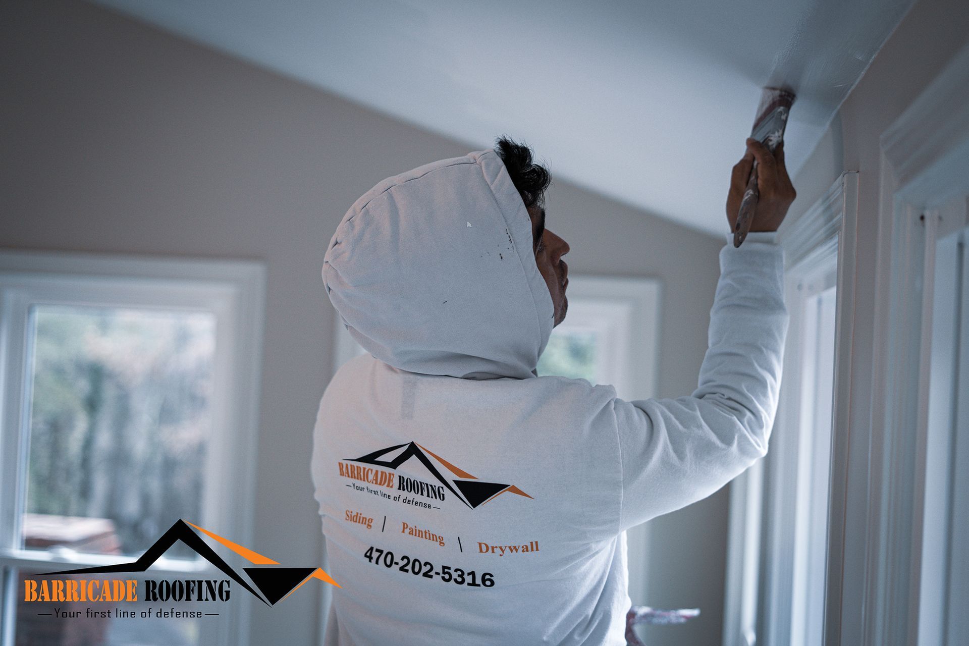 Person painting white trim indoors, wearing a hoodie with logo.