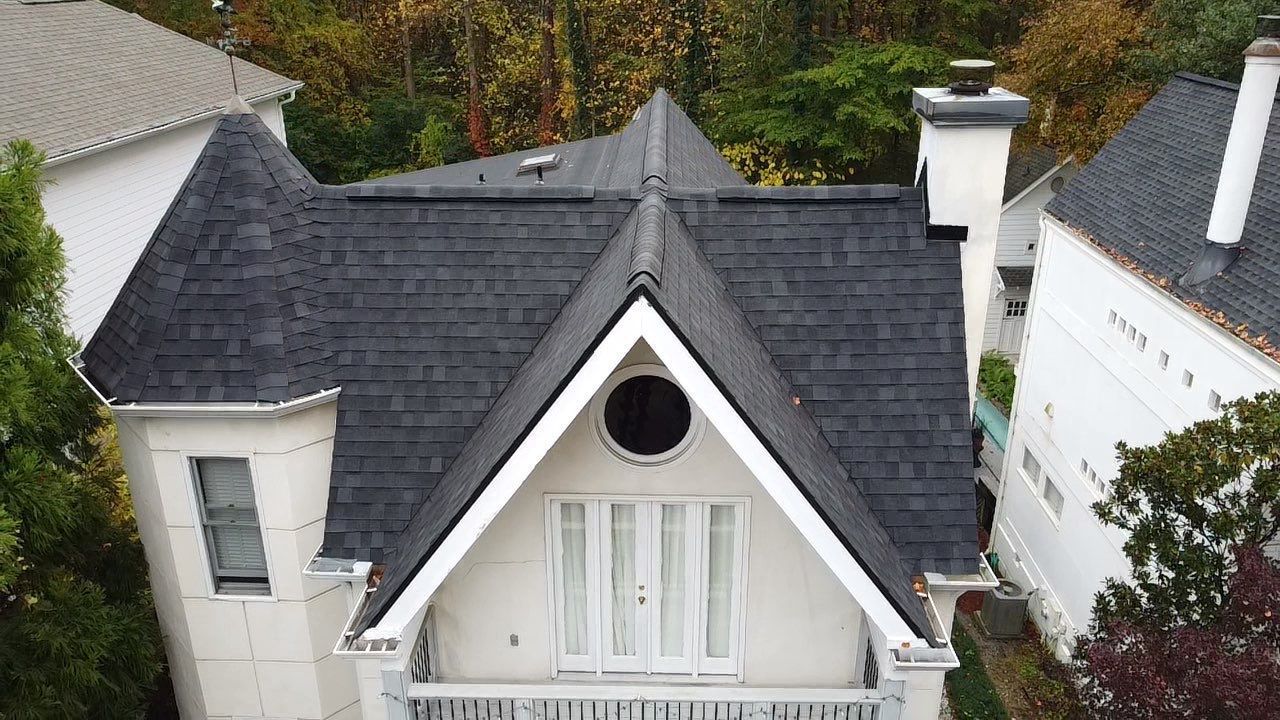 White house with a dark, complex roof, with a circular window and turret.