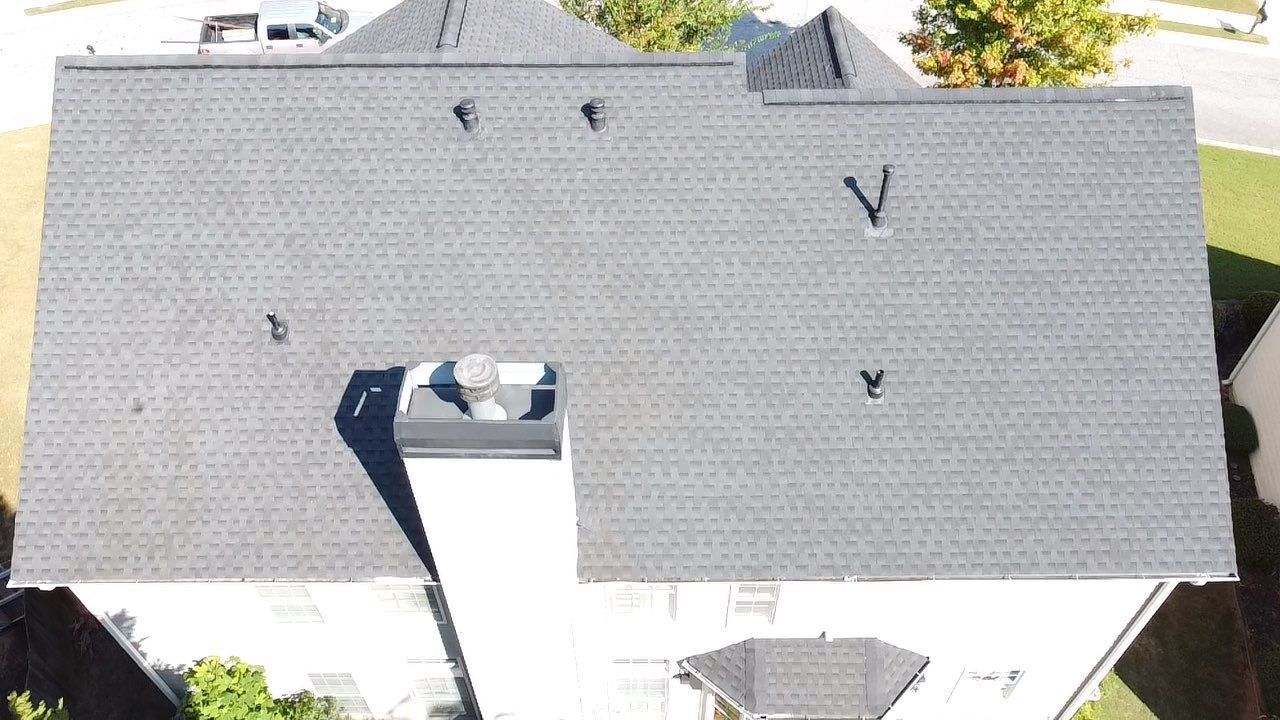 Overhead view of a house roof with gray shingles, vents, and a chimney.