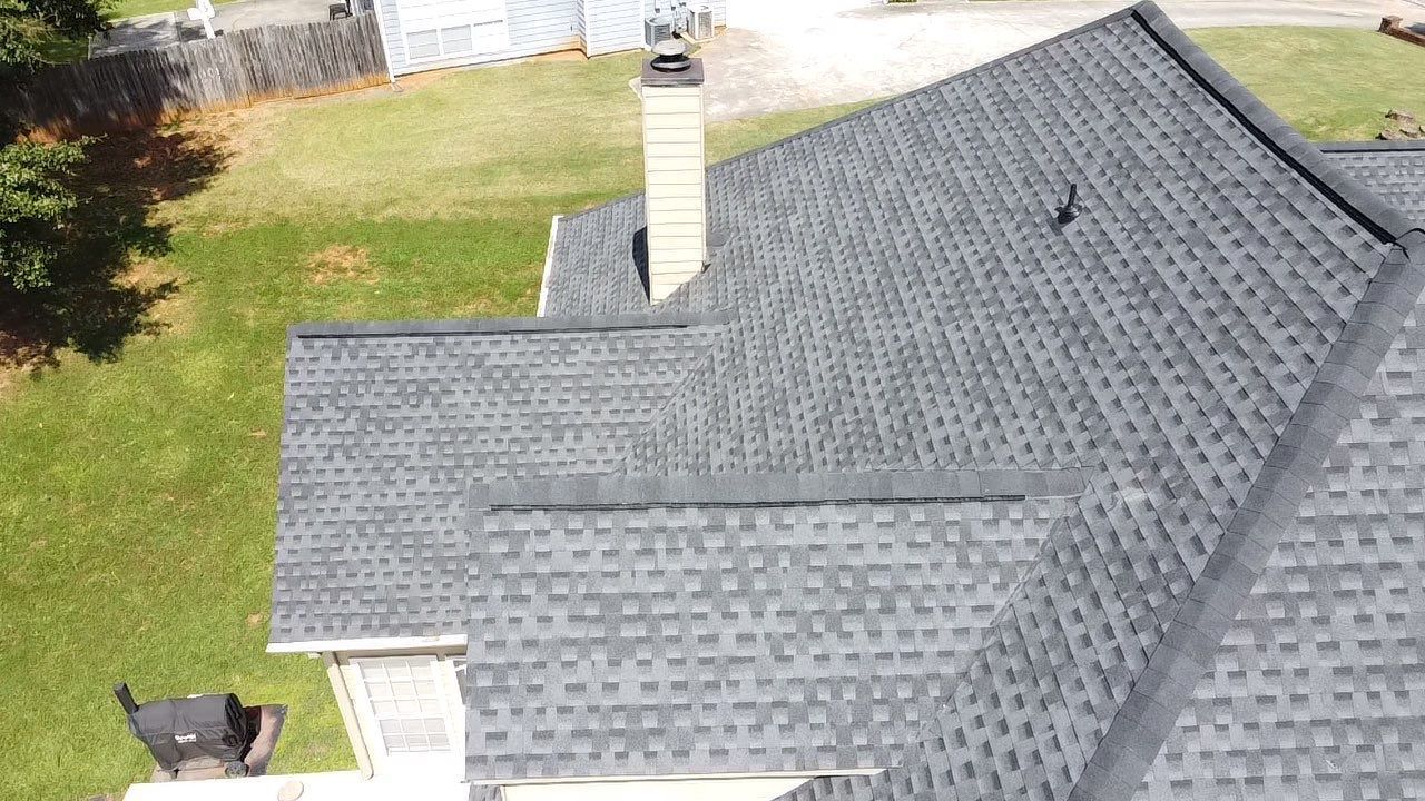 Dark gray asphalt shingle roof on a house with a brick chimney, viewed from above.