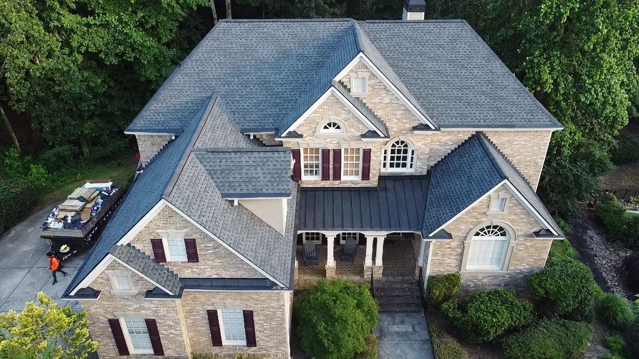 Multi-story brick house with gray roof, front porch, and landscaping. A truck is parked in the driveway.