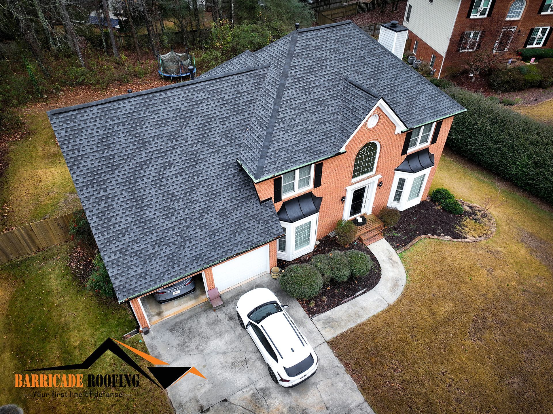 An aerial view of a two-story brick home with a gray shingle roof, white trim, and a car parked in the driveway.