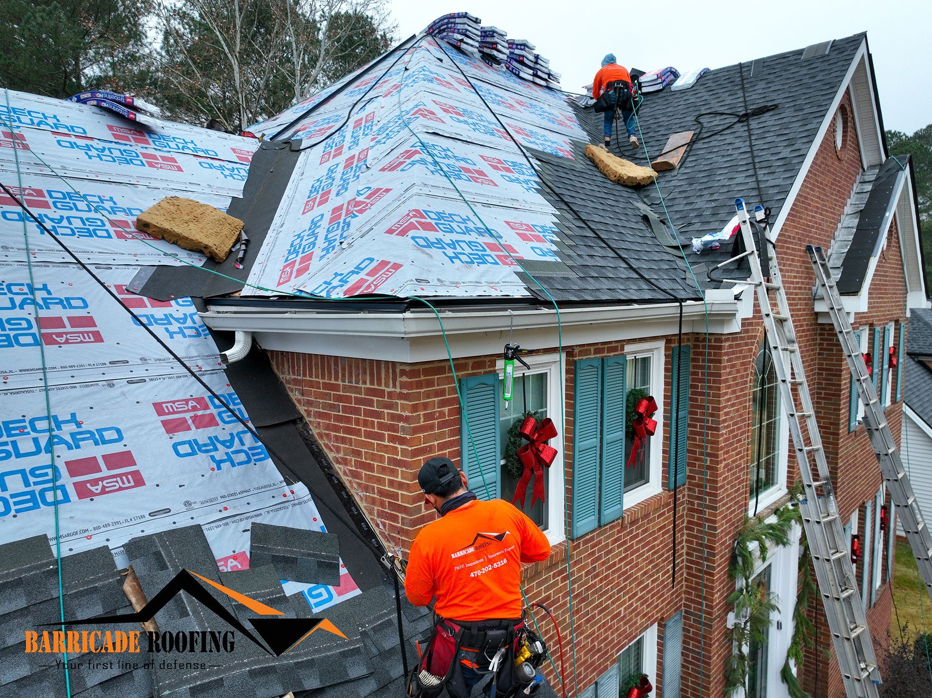 Roofers working on a brick house, installing roofing materials.