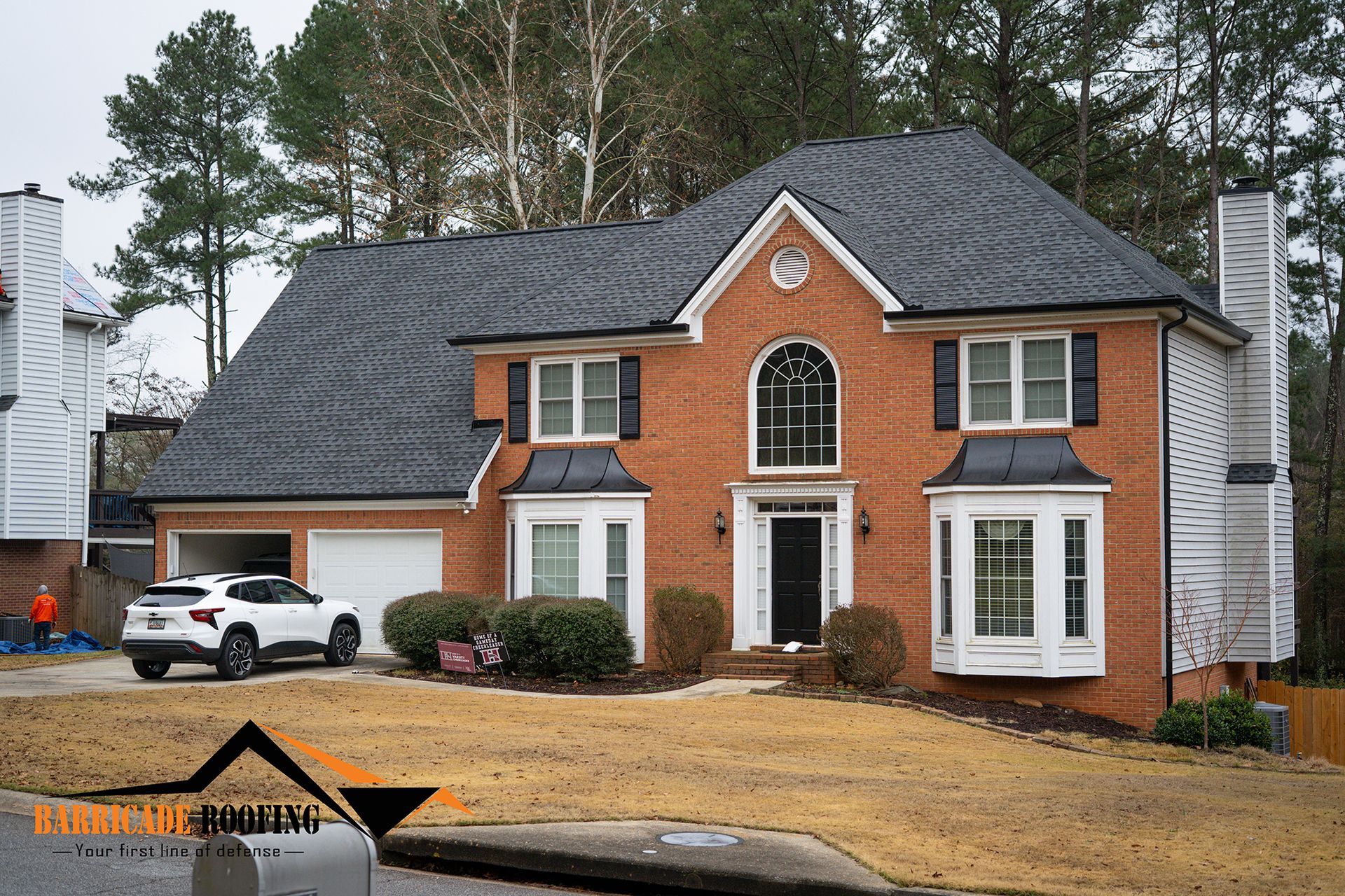 Brick house with dark roof, white trim, bay windows, and a white SUV parked in the driveway.