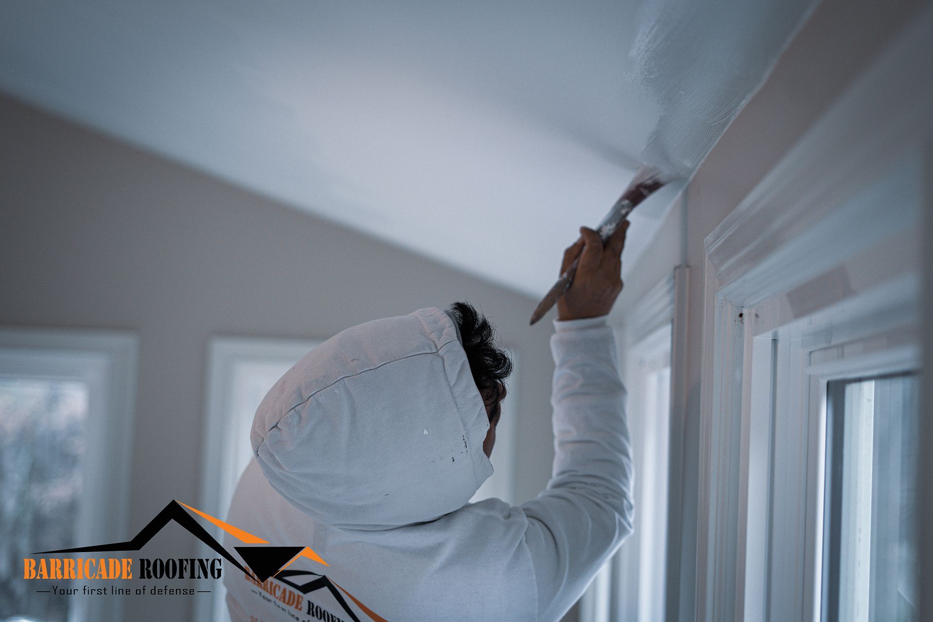 Person in white protective suit painting a white ceiling trim.