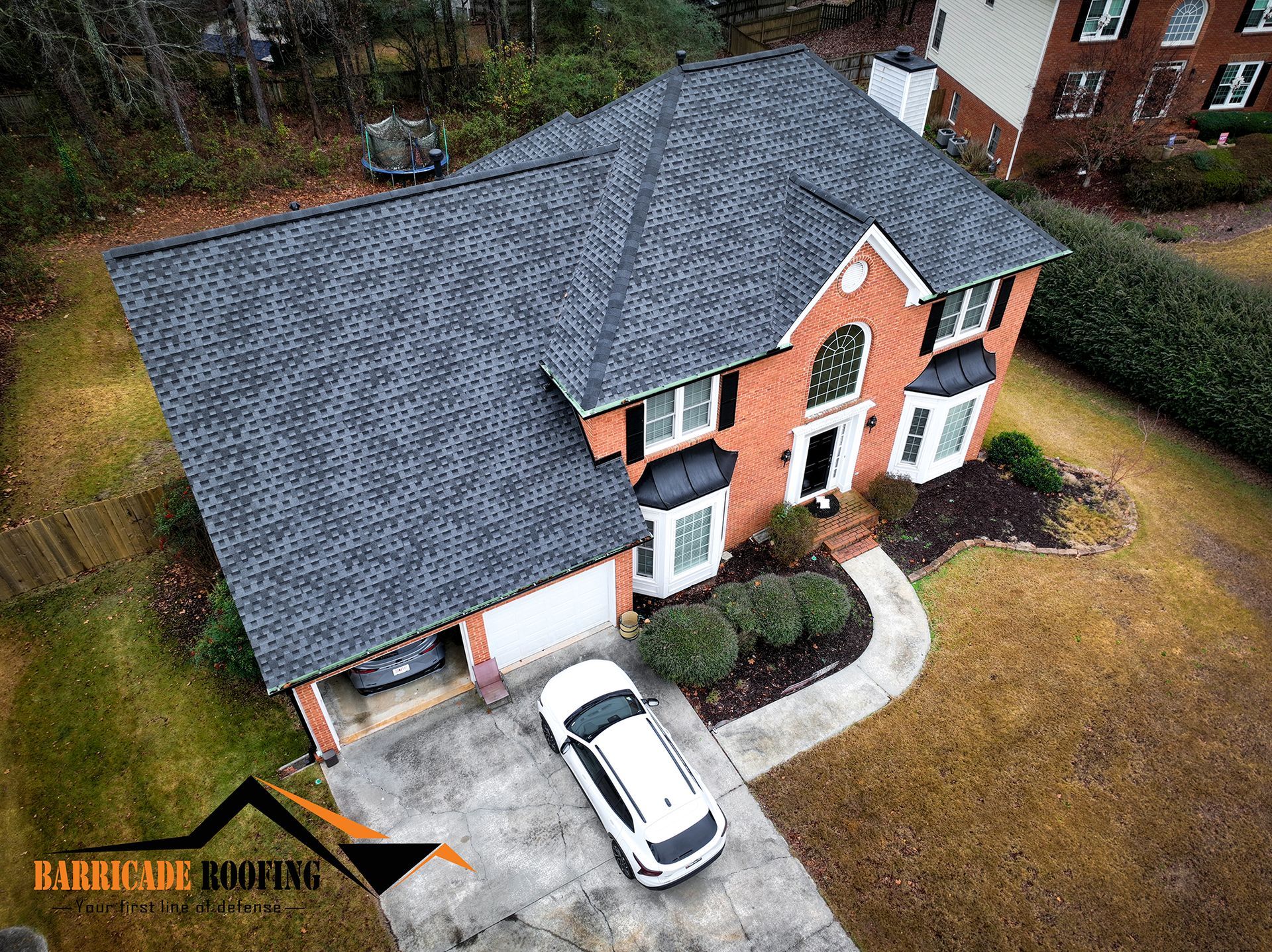 Aerial view of a two-story brick house with a dark gray roof, a white car in the driveway, and a well-manicured lawn.