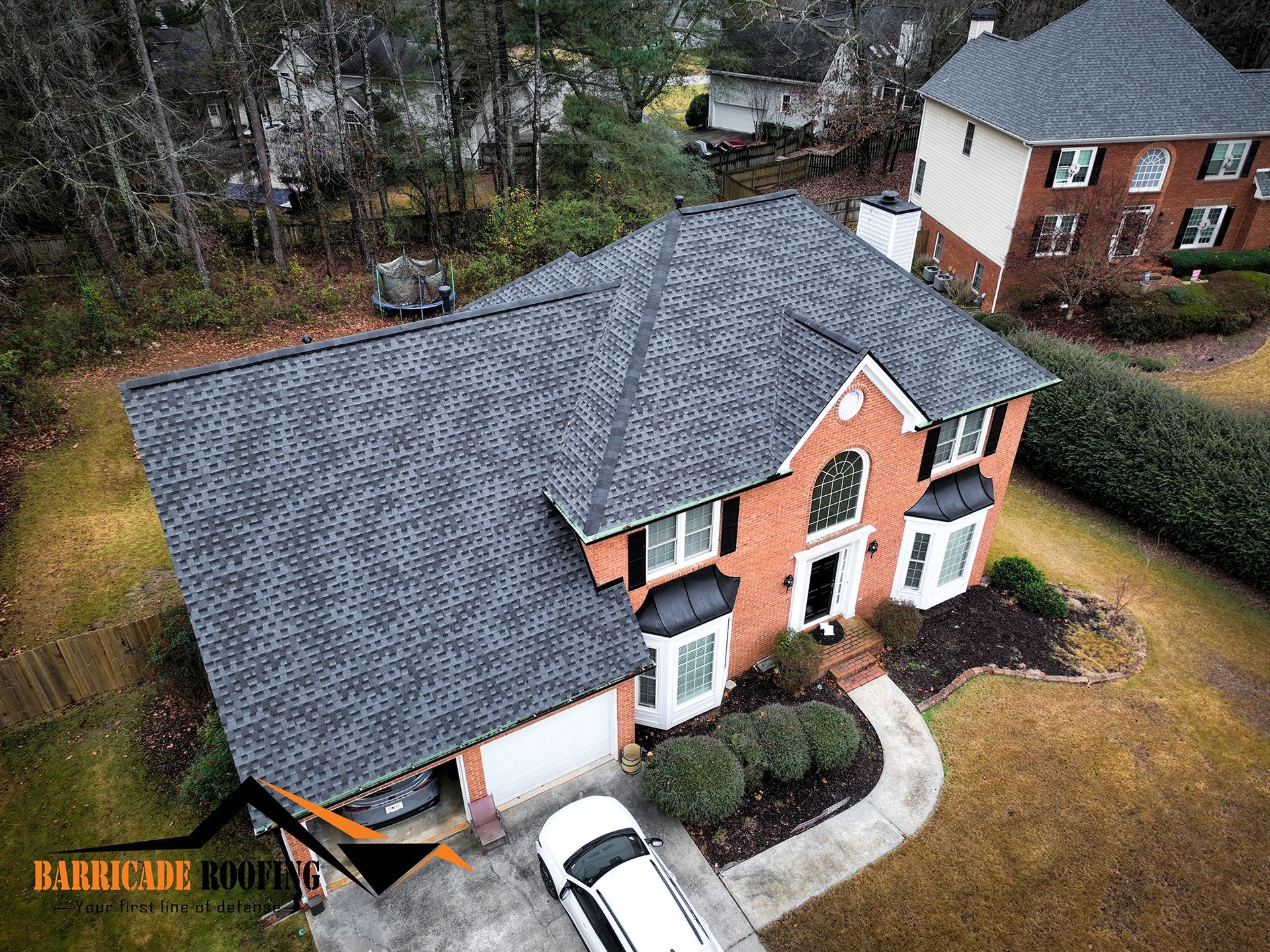 Aerial view of a two-story brick house with a dark gray shingle roof, white trim, and a white car parked in the driveway.