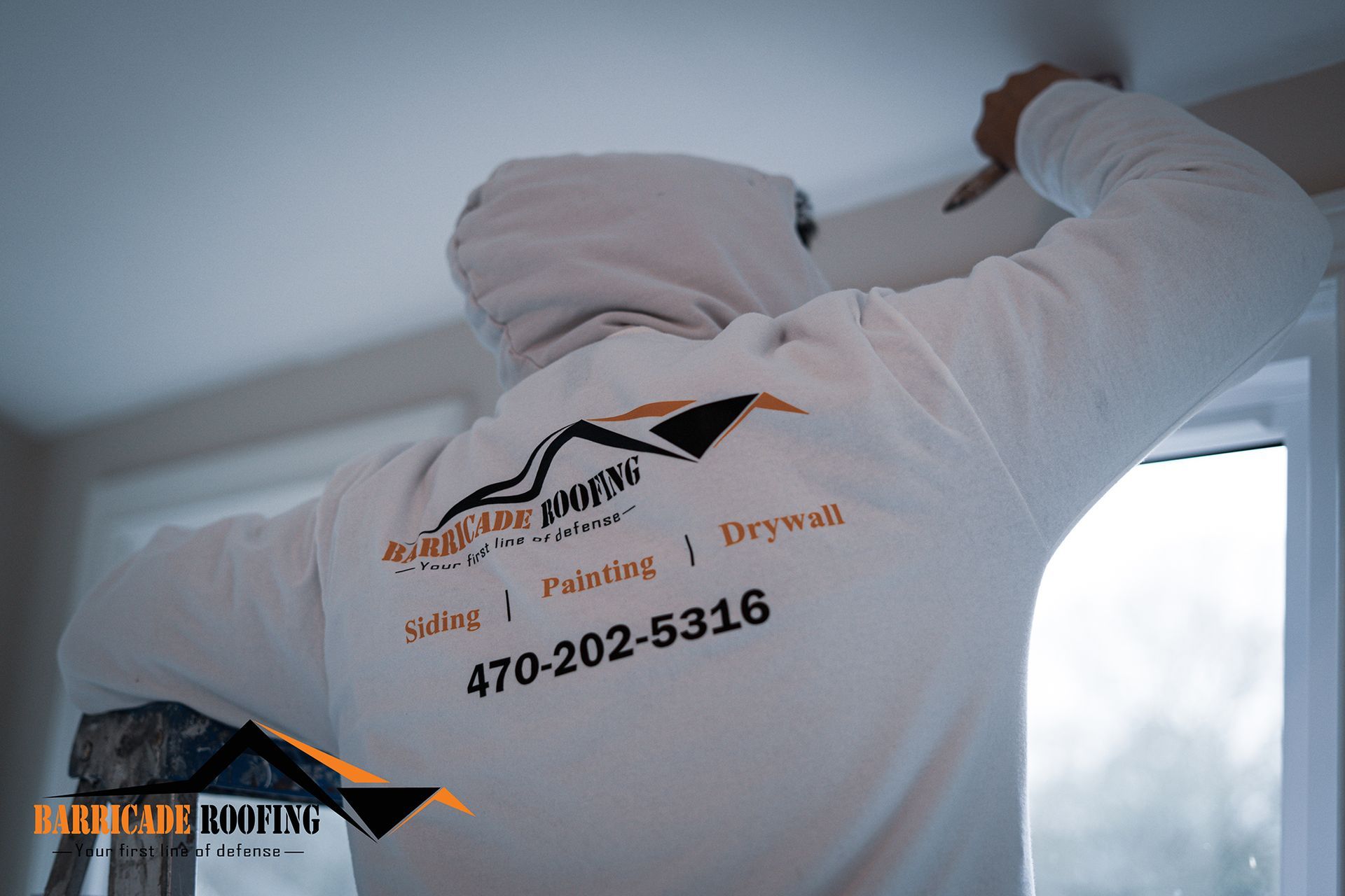 Person in a white hoodie working on a ceiling. The hoodie has a logo with a phone number on the back.