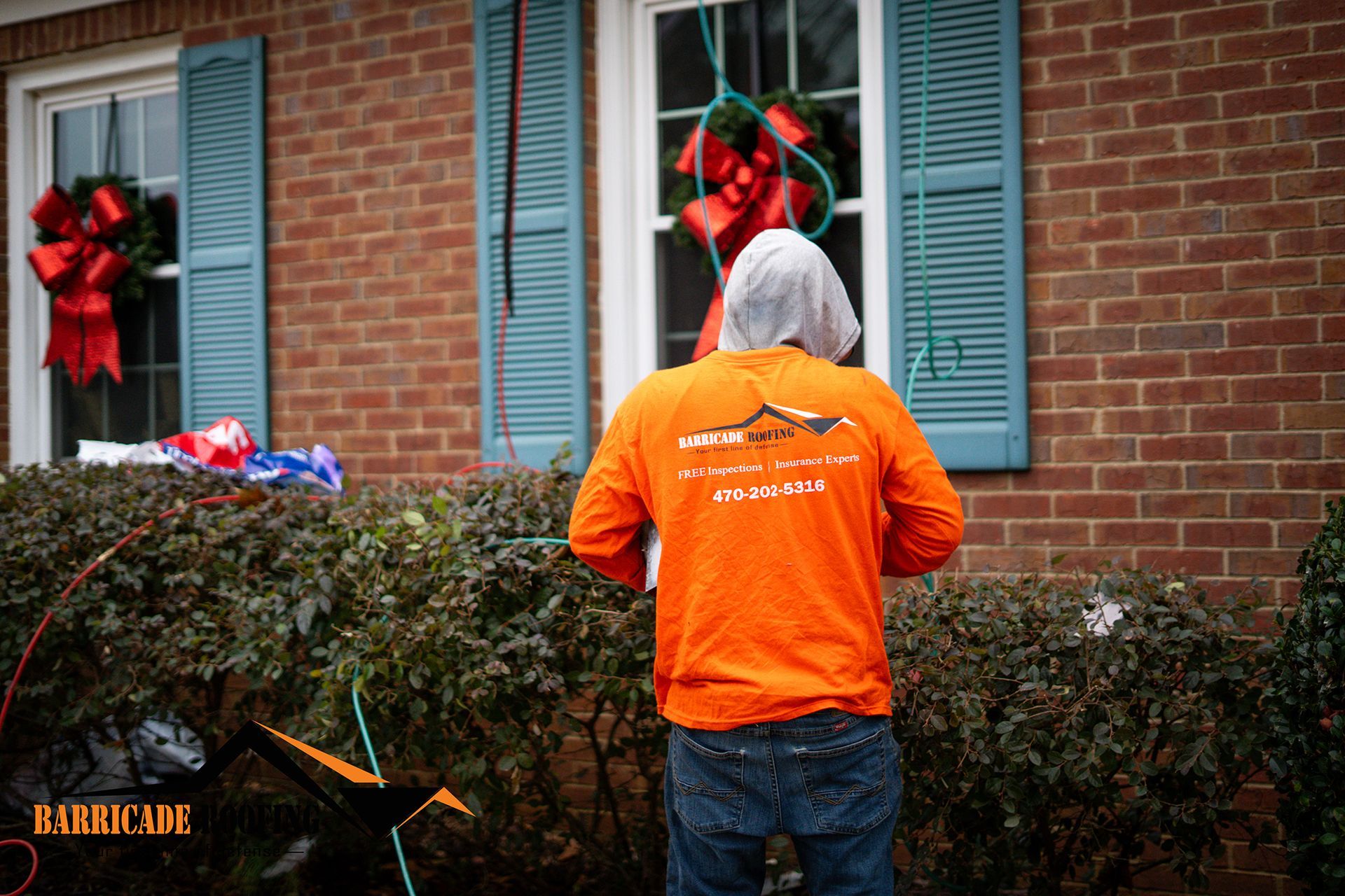 Person in orange shirt near brick house with Christmas decorations.
