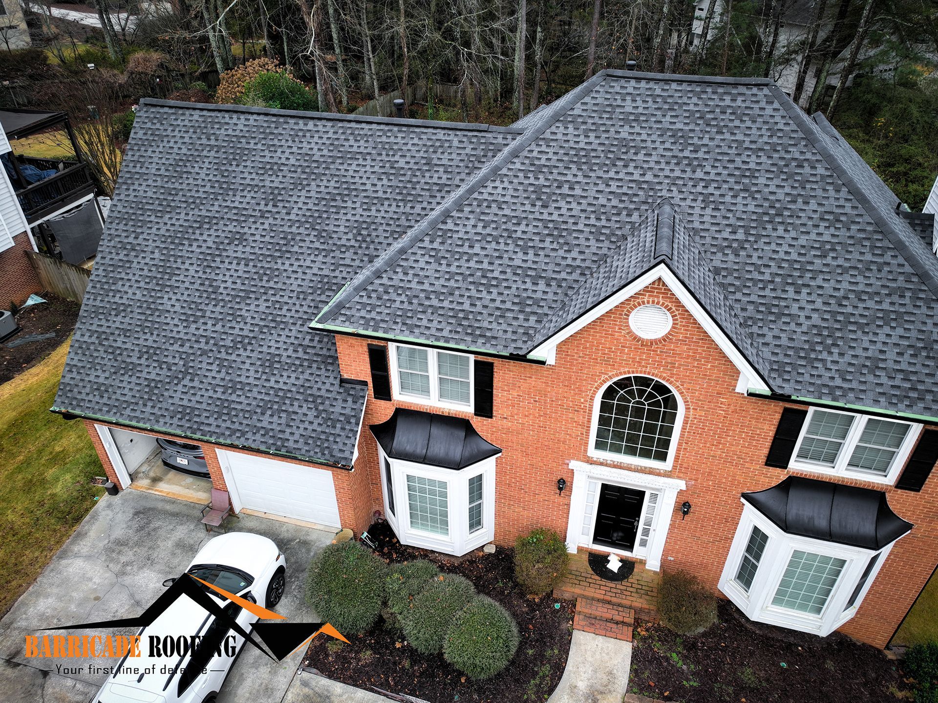 Aerial view of a brick house with a dark gray shingled roof, white trim, and black shutters.