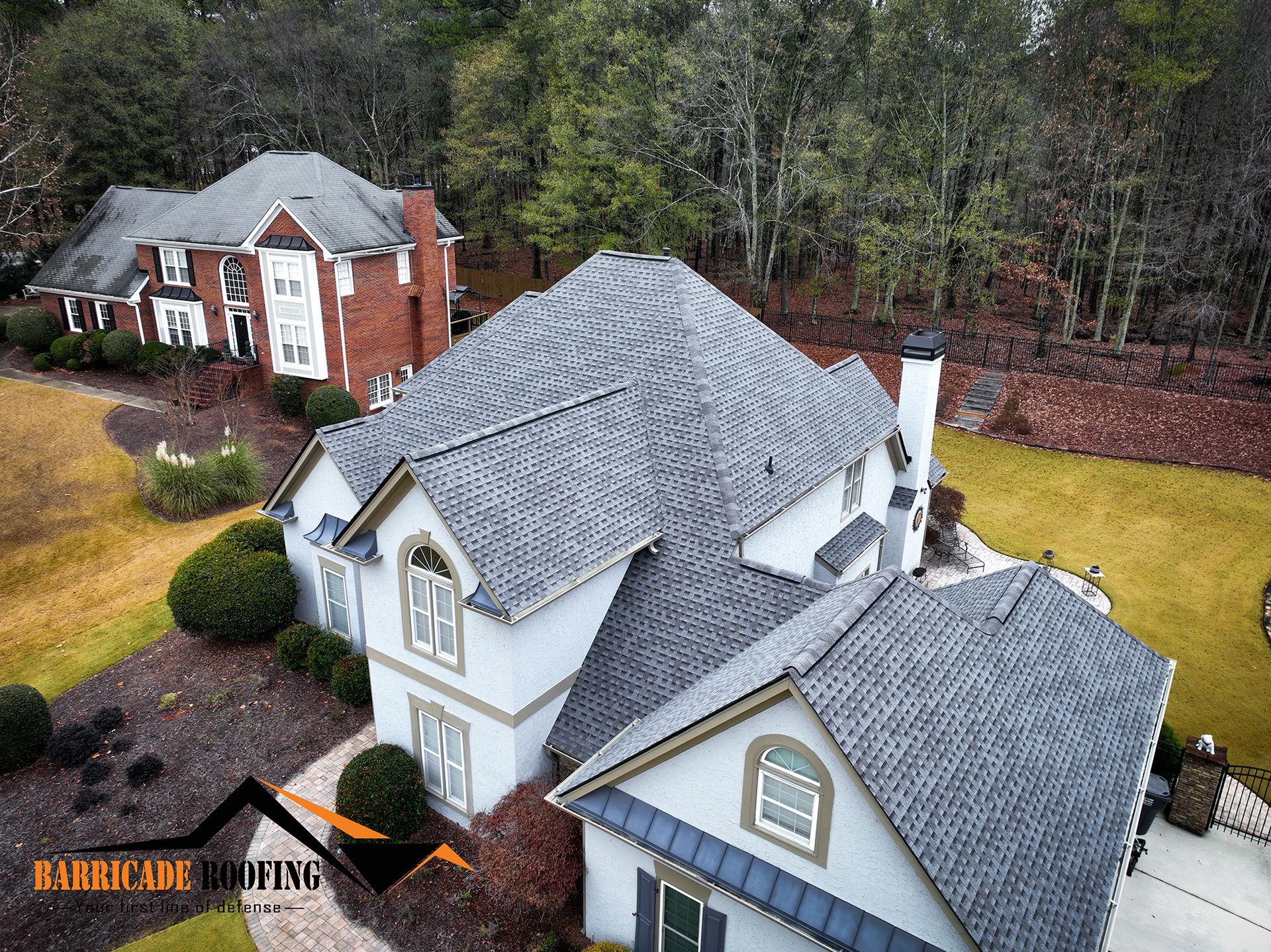 Aerial view of two houses with gray roofs. One house is brick. The other is white with green accents.