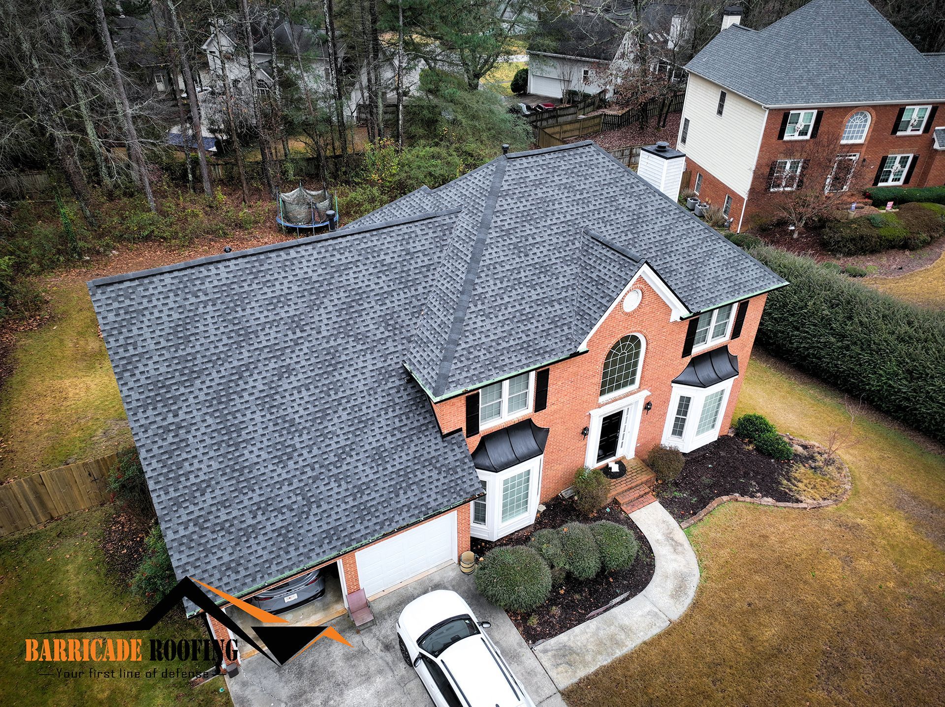 Aerial view of a two-story brick house with a gray shingle roof and a white car in the driveway.