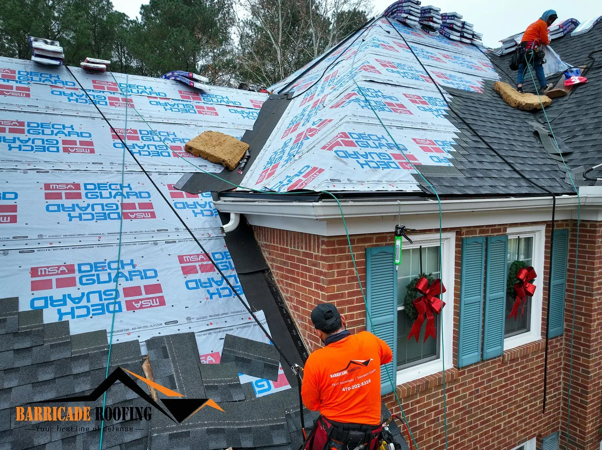 Roofers installing shingles on a brick house; safety harnesses used.