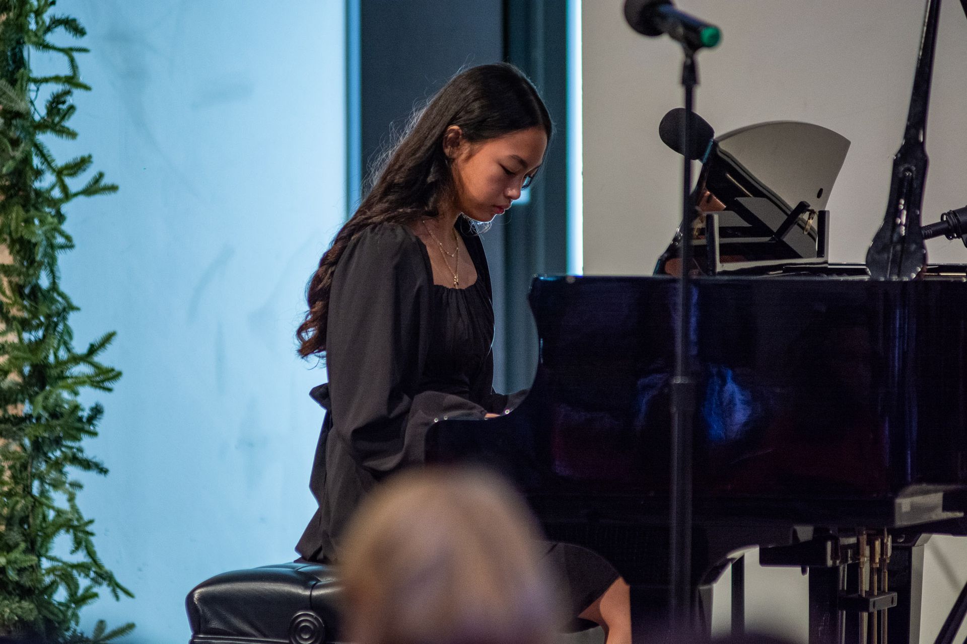 A woman in a black dress is playing a piano in front of a microphone.