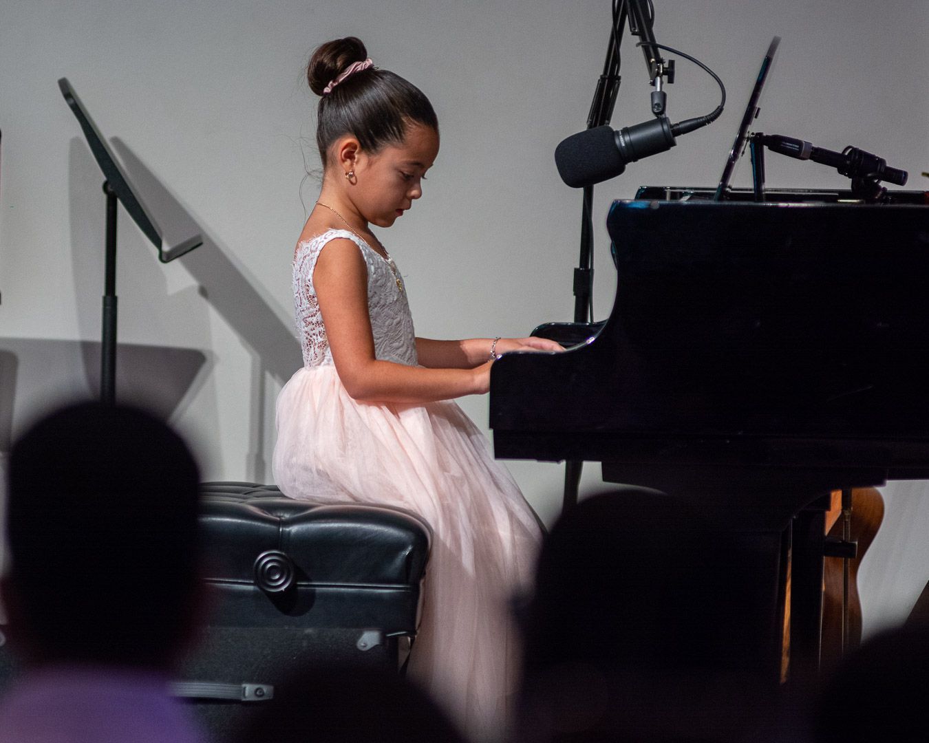 A little girl in a pink dress is playing a piano in front of a microphone.