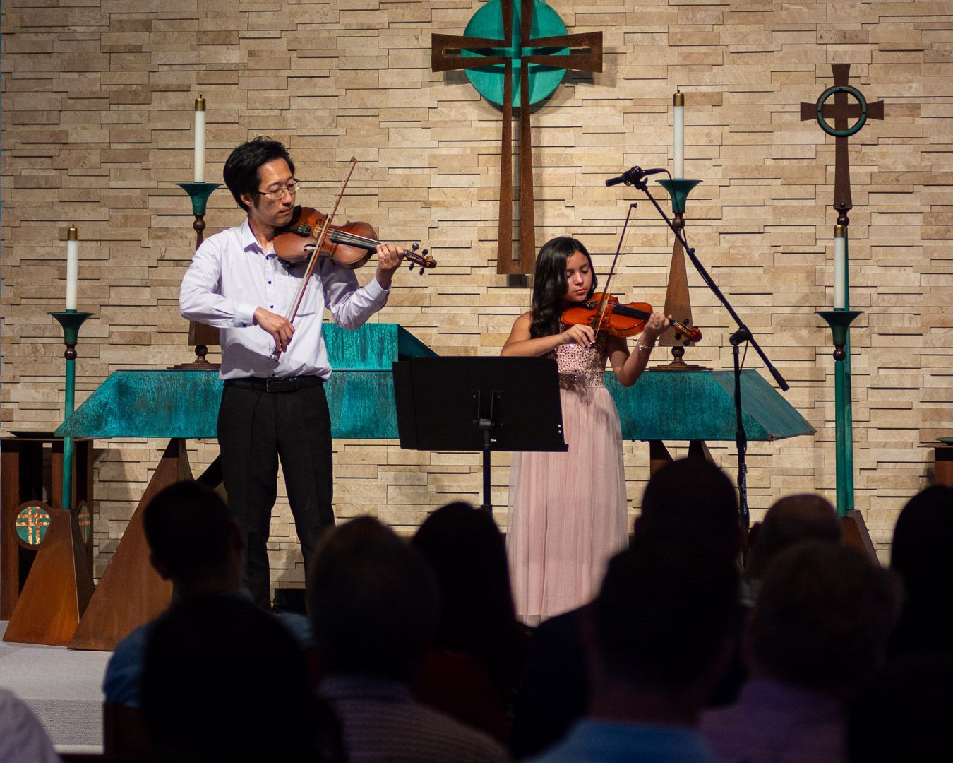 A man and a woman are playing violins in front of a crowd in a church.