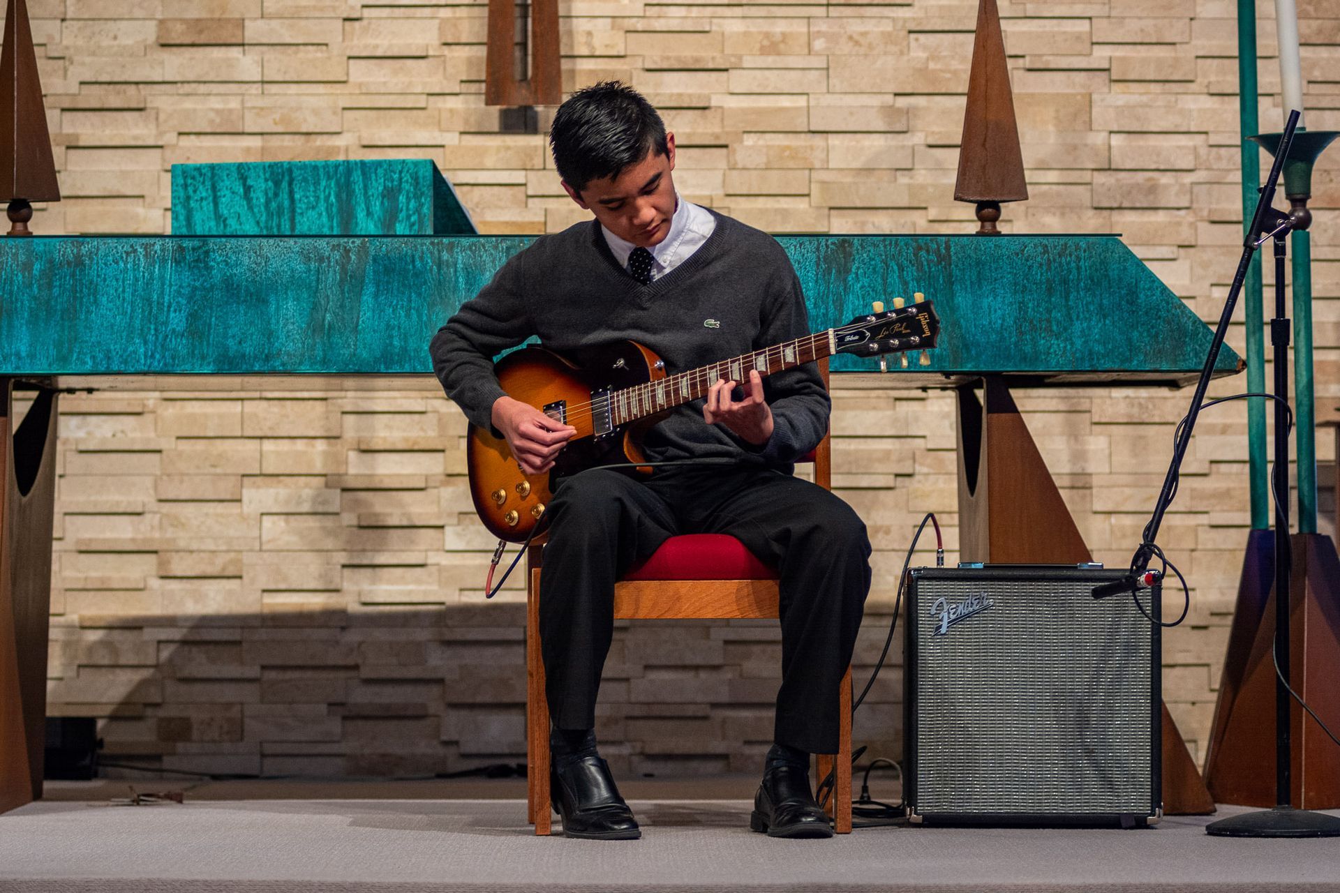 A young man is sitting in a chair playing an electric guitar in a church.
