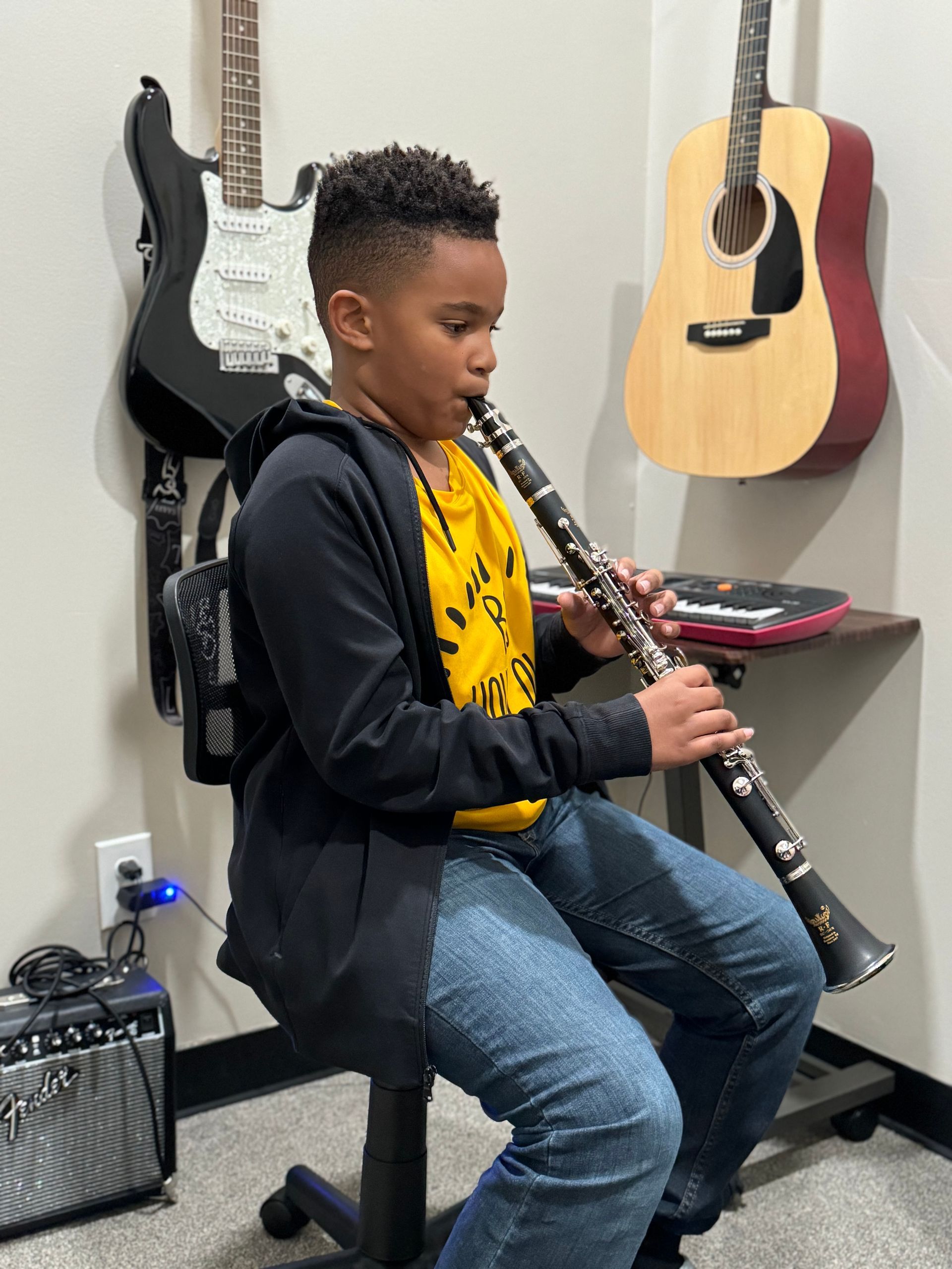 A young boy is playing a clarinet in a room with guitars hanging on the wall.