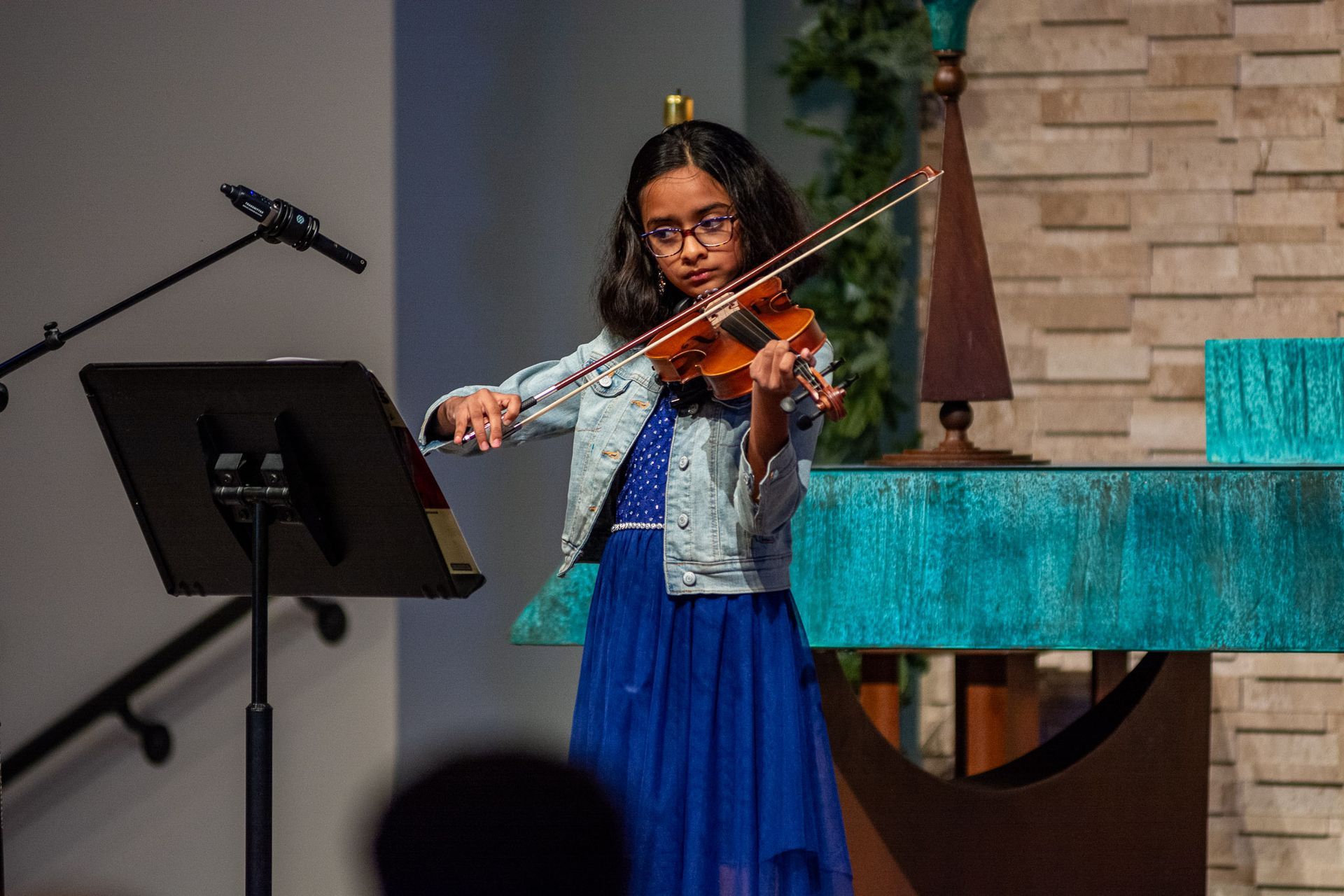 A young girl is playing a violin on a stage.