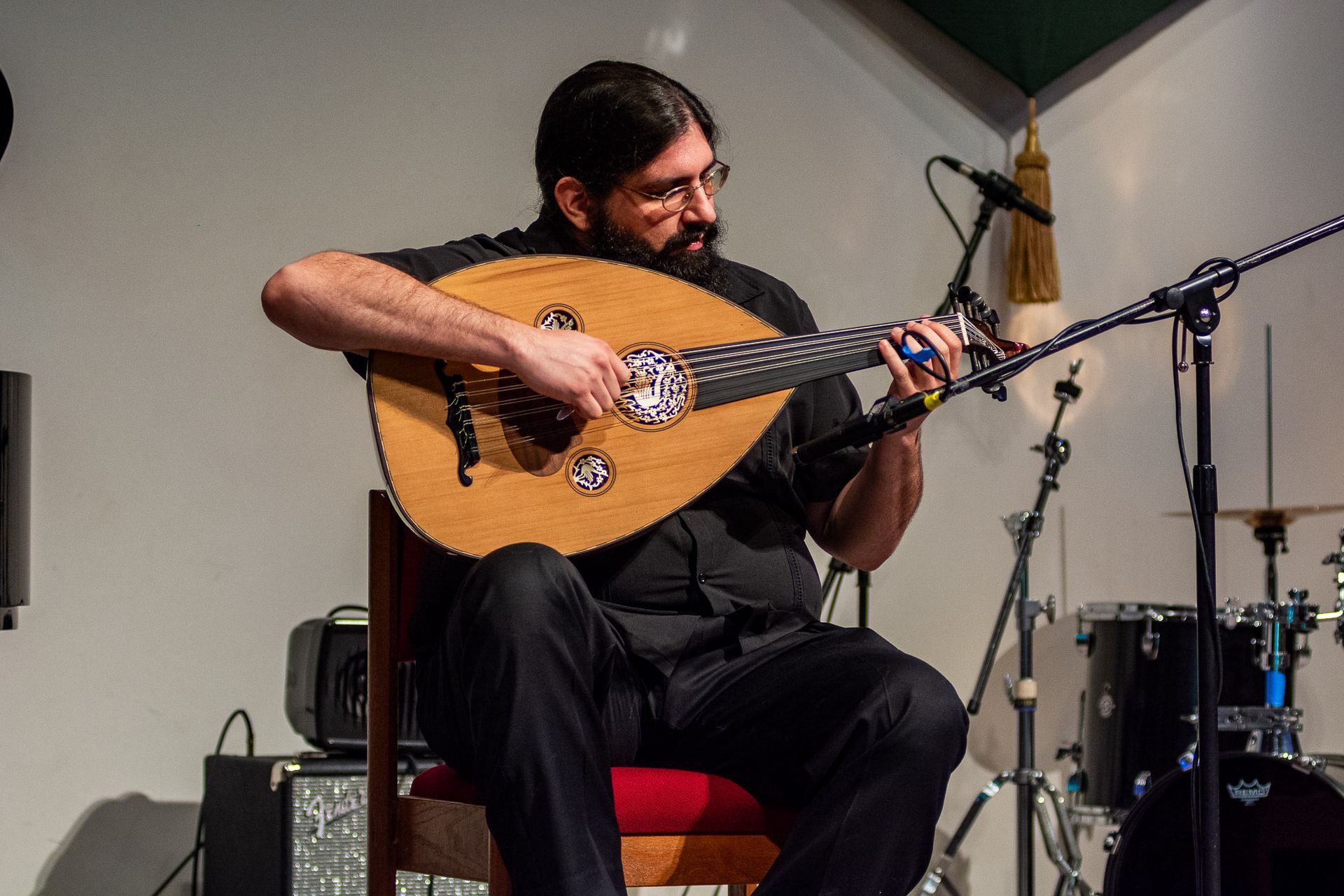 A man is sitting in a chair playing a guitar in front of a microphone.